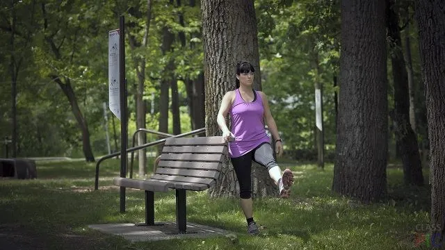 Девушка делает зарядку в парке у скамейки