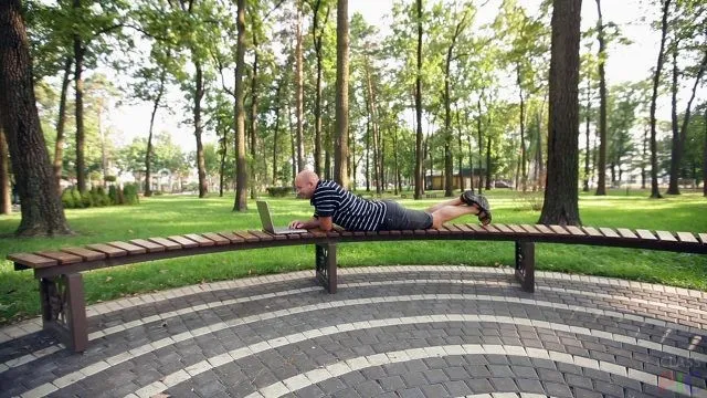 Мужчина с ноутбуком лежит на парковой скамейке