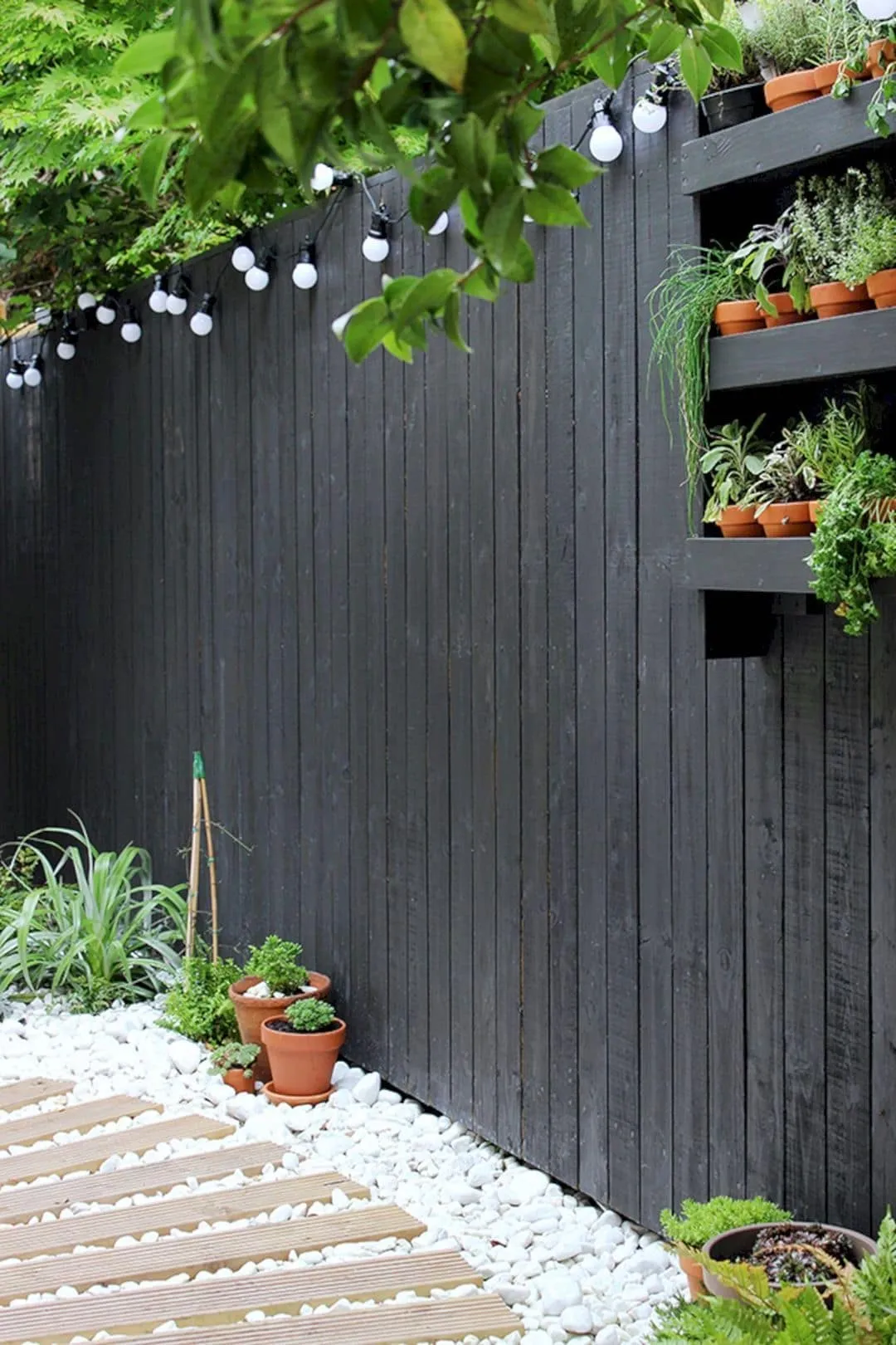 Забор из дерева, окрашенный в темный или даже черный цвет, подчеркнут белые камешки и яркая подсветка 